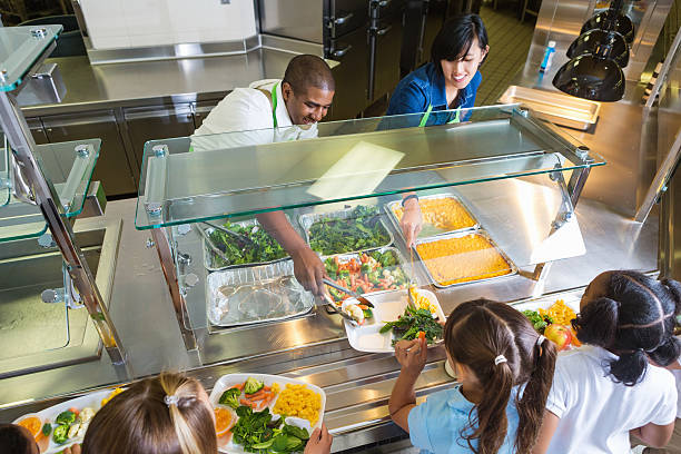 Cafeteria+worker+serving+trays+of+healthy+food+to+children