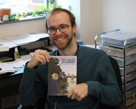 Kevin Rinald holding his copy of, They Called Us Enemy, in his classroom.