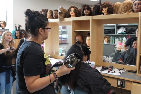Students in their first year of cosmetology attempting a blow out on a manikin and other classmates.