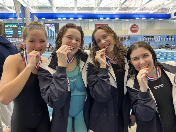 Lila Kate Robinson, Alex Fuller,  Reece Yowell, and Sophie Pace bite their medals after the State Championship meet on February 17, 2024. Photo courtesy of Mitchell Pace.
