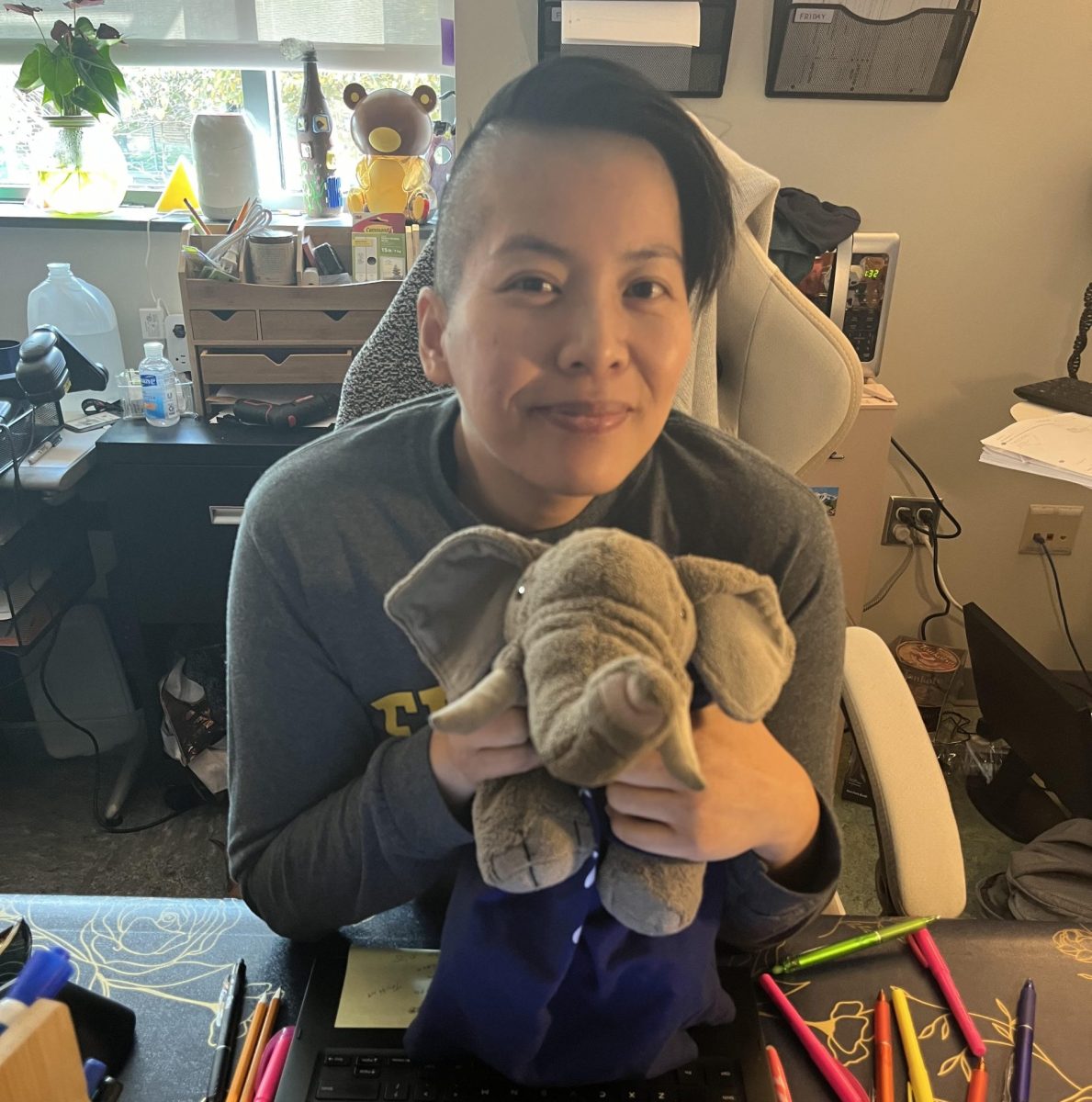 Amanda Fisher hugging elephant stuffed animal sitting down behind her desk.