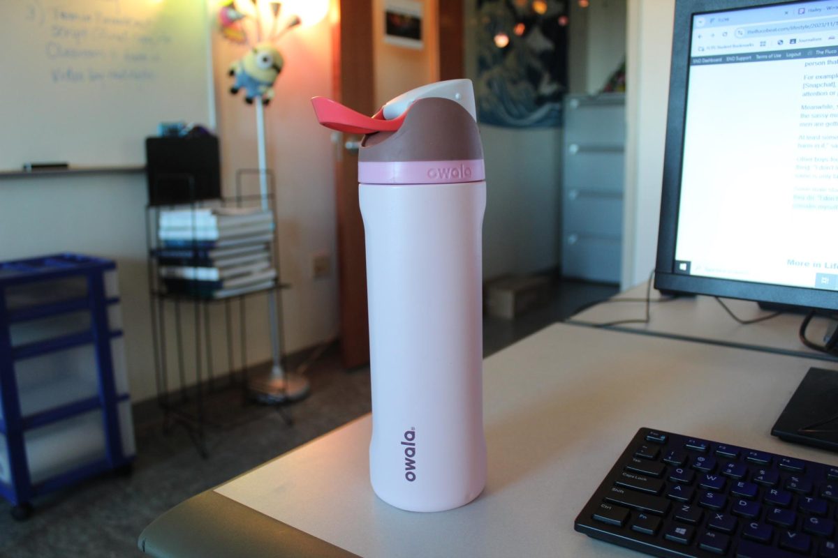 A pink Owala water bottle sits on the desk.