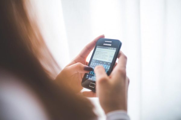 A person holding a smart phone in their hands. with their fingers tapping on the screen. Photo courtesy of Kaboompics through Creative Commons CC0 https://freerangestock.com/photos/77711/person-holding-a-smart-phone.html