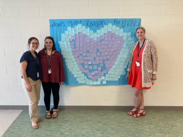 Jessica Lavin, Brianna McBride, and Emily Primm, all sponsors of Sources of Strength, stand next to a poster made by the SOS club.