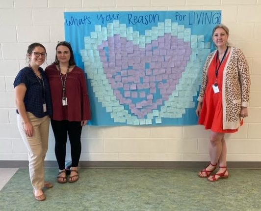 Jessica Lavin, Brianna McBride, and Emily Primm, all sponsors of Sources of Strength, stand next to a poster made by the SOS club.