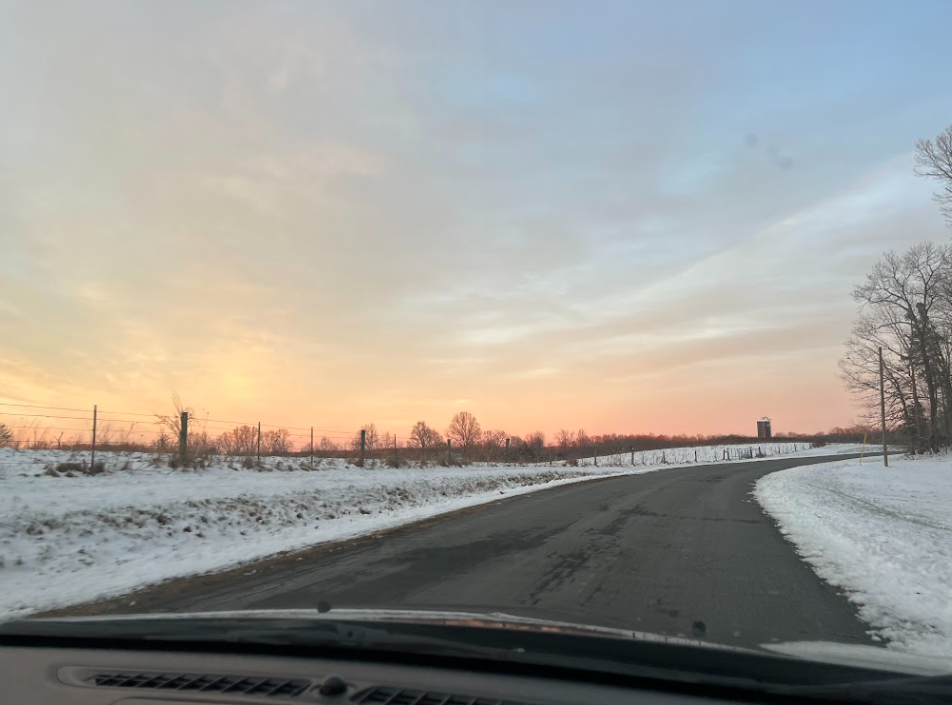 Photo of sunset with snow on the edges of a road.