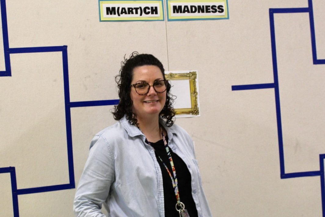 Art teacher Michelle Coleman in front of a previous year's M(art)ch Madness bracket board outside of her classroom. 