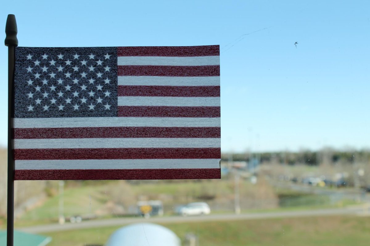 A closeup photo of the American flag with the back of Fluvanna County High School blurred in the background.