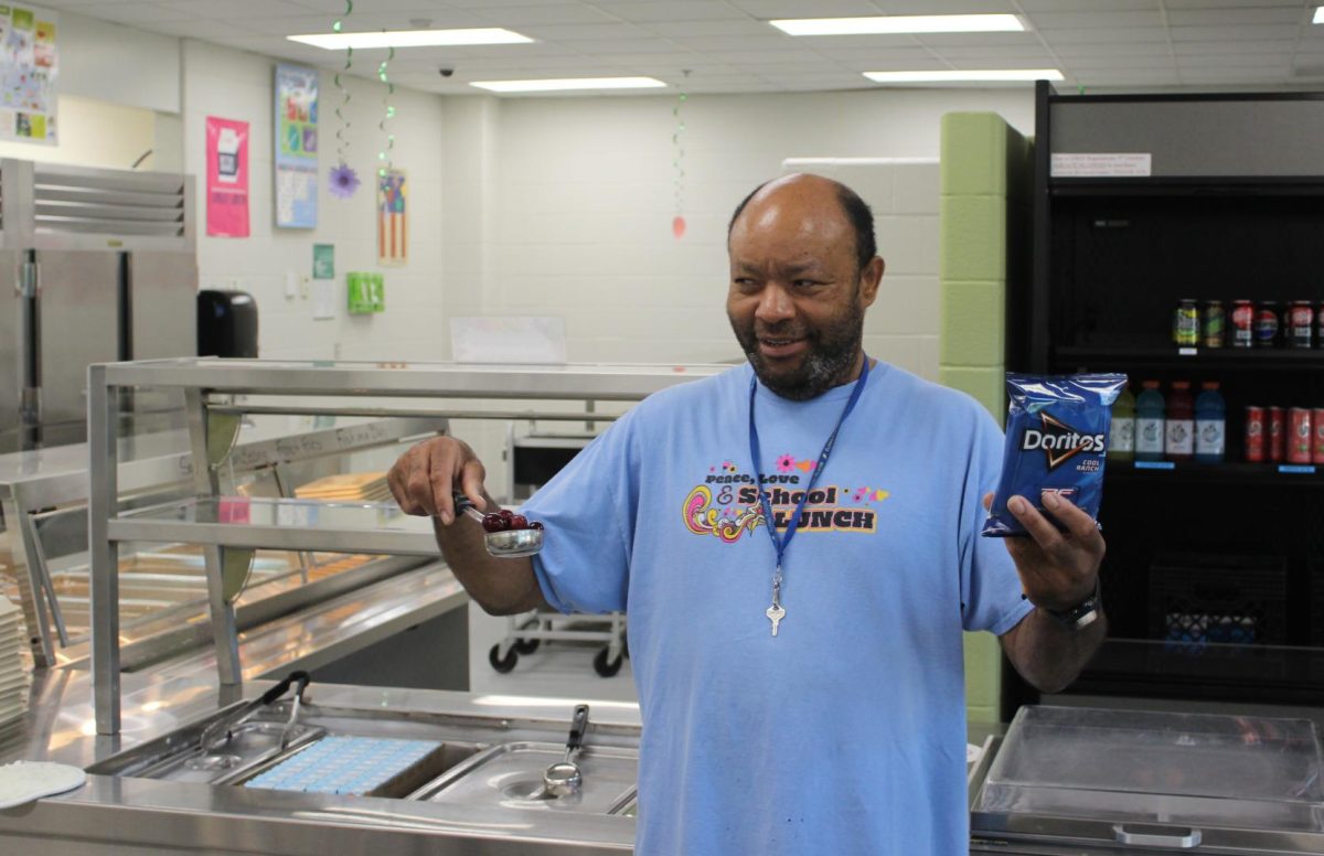 Mr. Charlie holding a cup of grapes and a bag of chips in the cafeteria.